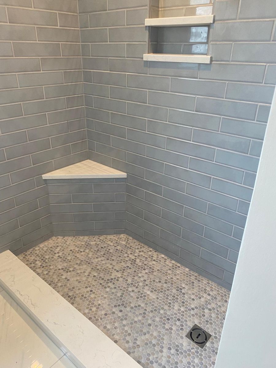 Blue subway tile shower with corner bench and hex tile floor